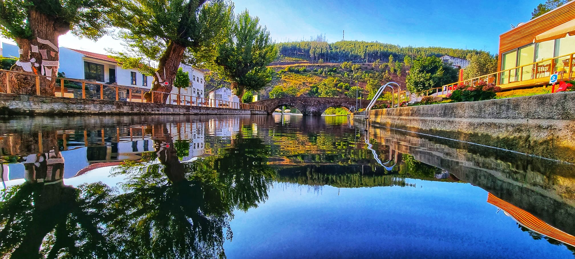 Praia fluvial de Alvares com ponte de pedra e reflexo na água
